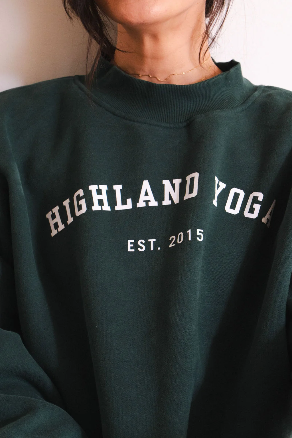 Close-up of the Highland Yoga Est. 2015 lettering on a forest-green sweatshirt